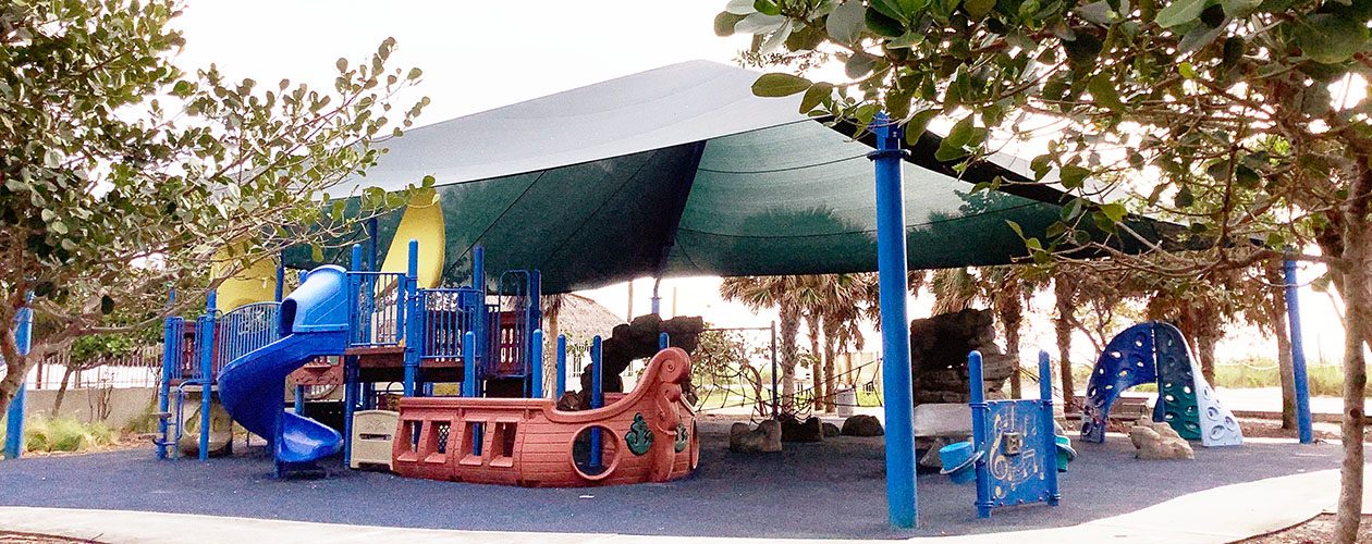 Ship-shaped playground under a large green shade canopy at Beach View Park