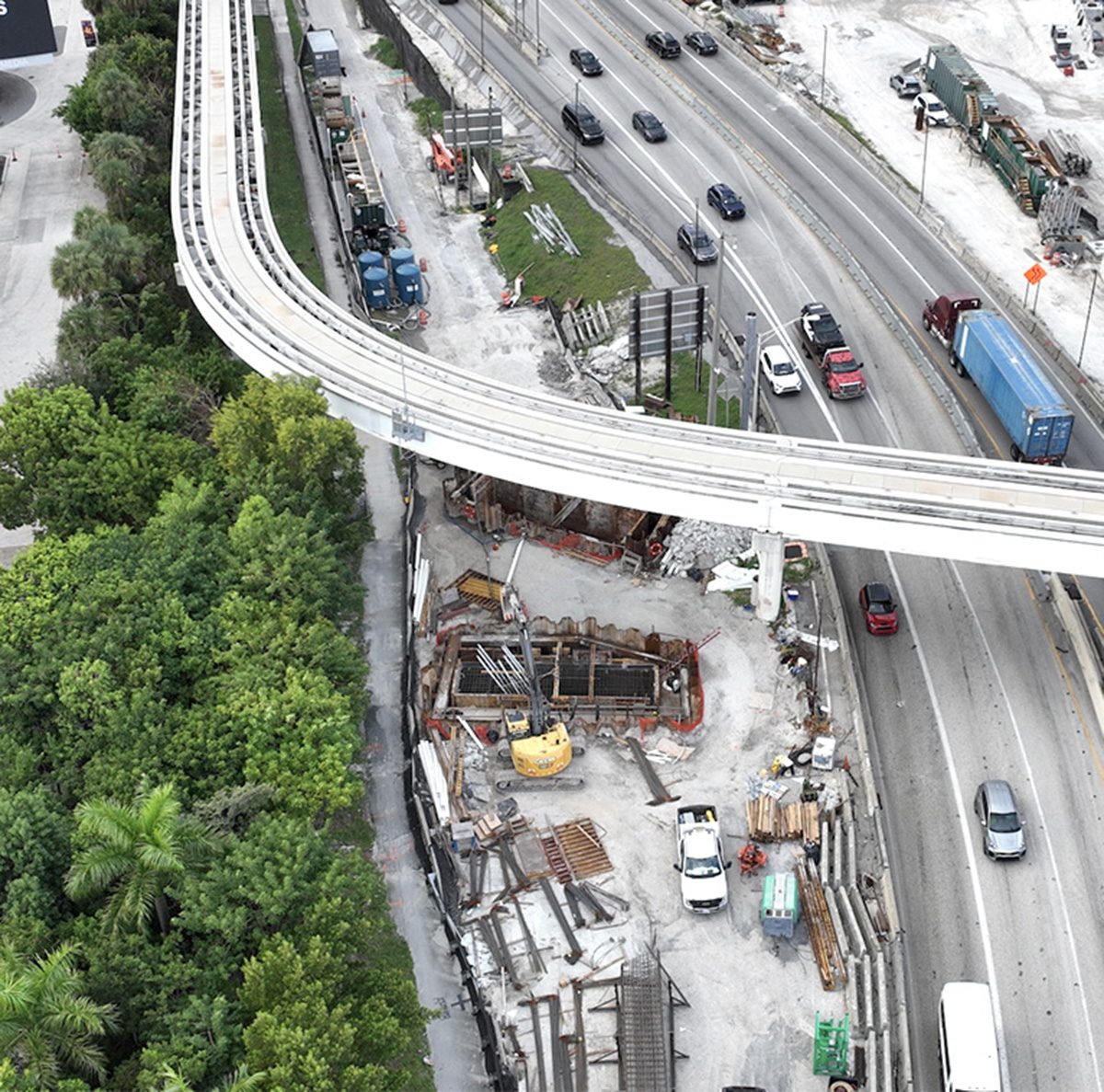 Aerial view of traffic on I-395 in downtown Miami passing a construction site beneath a curving Metromover guideway