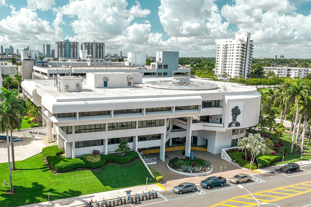 Aerial view of the white, curved Miami Beach City Hall building with palm trees and a lawn out front