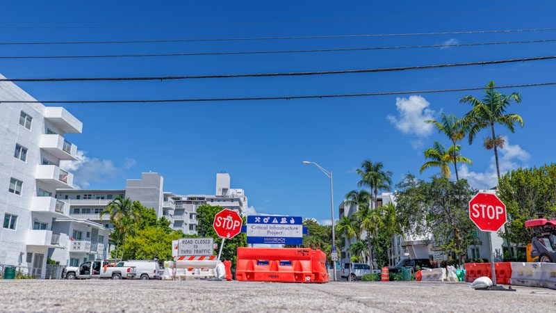 Road closed sign, stop signs and orange barriers at a West Avenue project work zone, with a Critical Infrastructure Project sign behind them